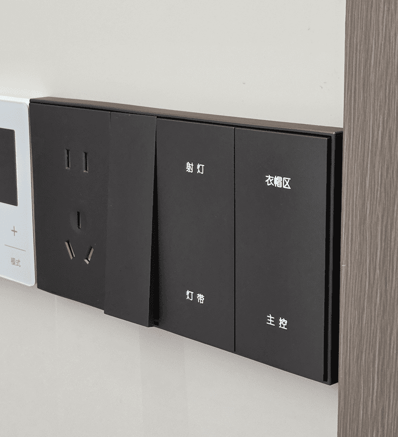 Real installation shot of 4-button black plastic smart wall switch, controls spot light, light strip, cloak area and master light, next to power socket