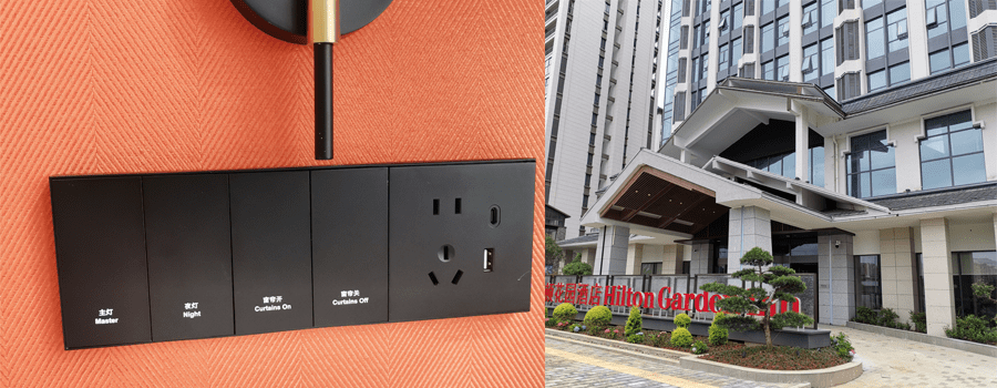 On-site installation photo of black eco painted plastic Zigbee smart switch panel for Hilton hotel project, integrated with 5-hole power socket, USB & Type-C charging port, 4 control buttons for master light, night light, curtain open and curtain close, mounted on orange textured wall fabric